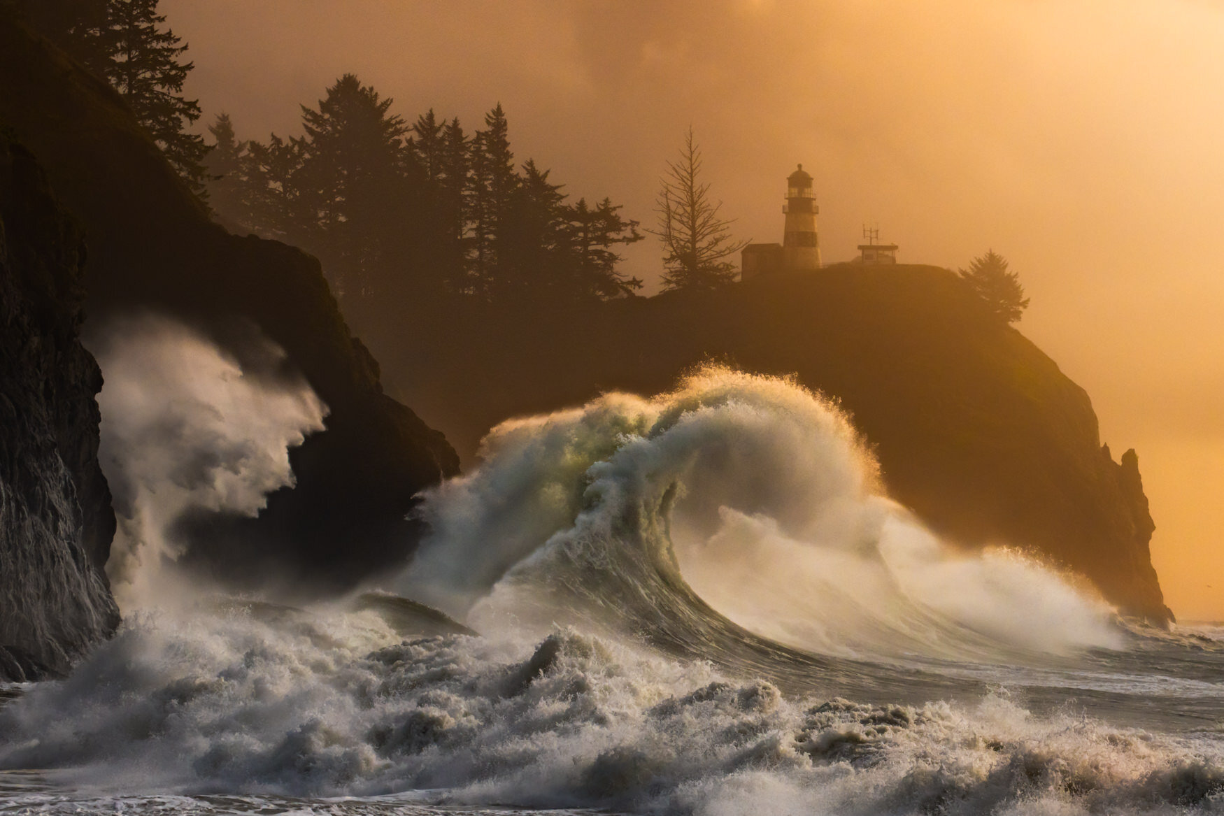 A large wave crashes over a lighthouse at Cape Disappointment in Washington during sunset - photographed by Chris Byrne. | Photo Title: Poseidon Awakes | 
        Photo by Chris Byrne ©2023