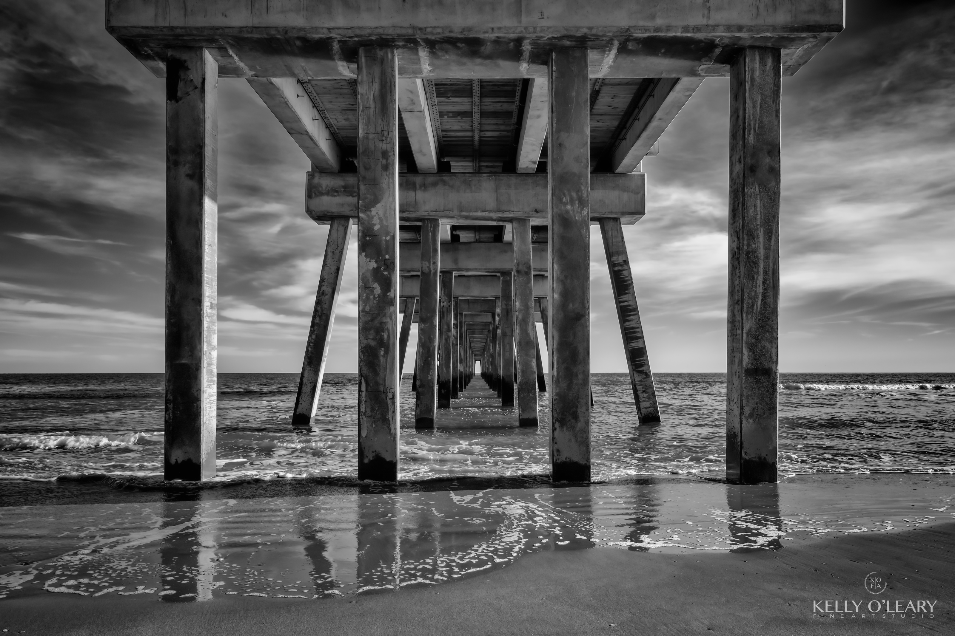 A black and white photograph impeccably captures the essence of a concrete pier, gently caressed by a tender tide, and bathed in the ethereal light of the evening. This arresting composition by Kelly metaphorically reveals the inherent stability that transcends time, inviting us to immerse ourselves in the artistry of not just the image, but also the emotions it evokes. | Photo Title: Stability | 
        Photo by Kelly O'Leary ©2023